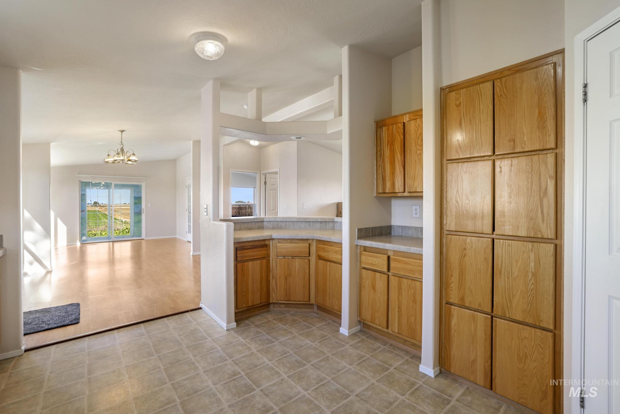 Kitchen with brown cabinetry, light countertops, a chandelier, open floor plan, and vaulted ceiling