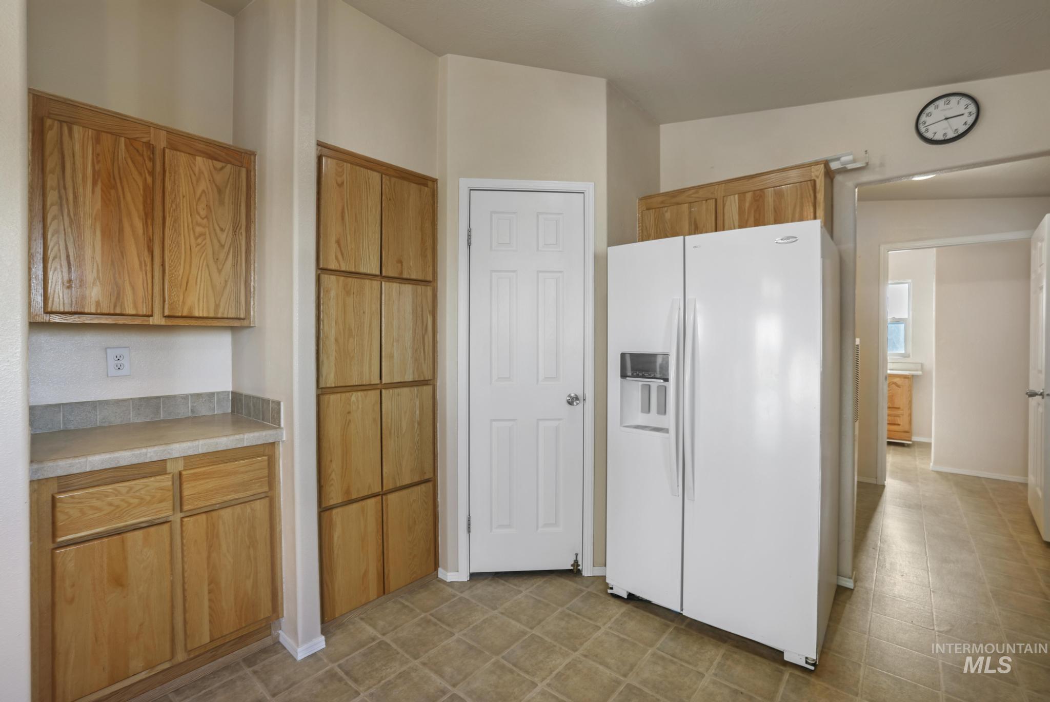 Kitchen featuring white fridge with ice dispenser, light countertops, and brown cabinets