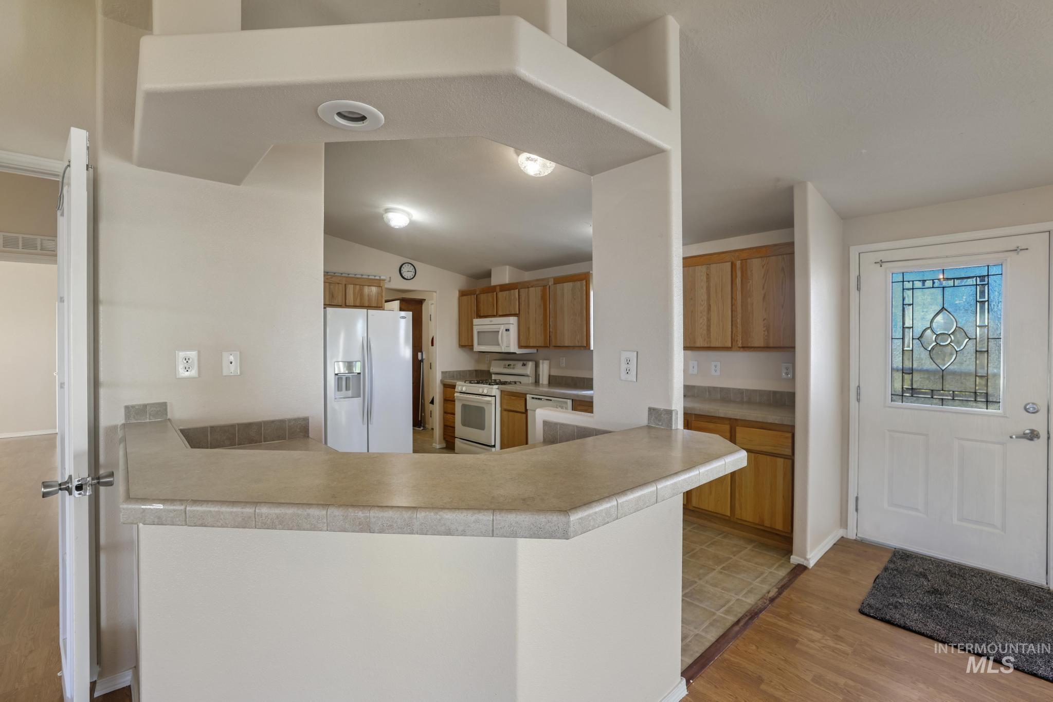 Kitchen with white appliances, light wood-style flooring, light countertops, brown cabinetry, and a peninsula