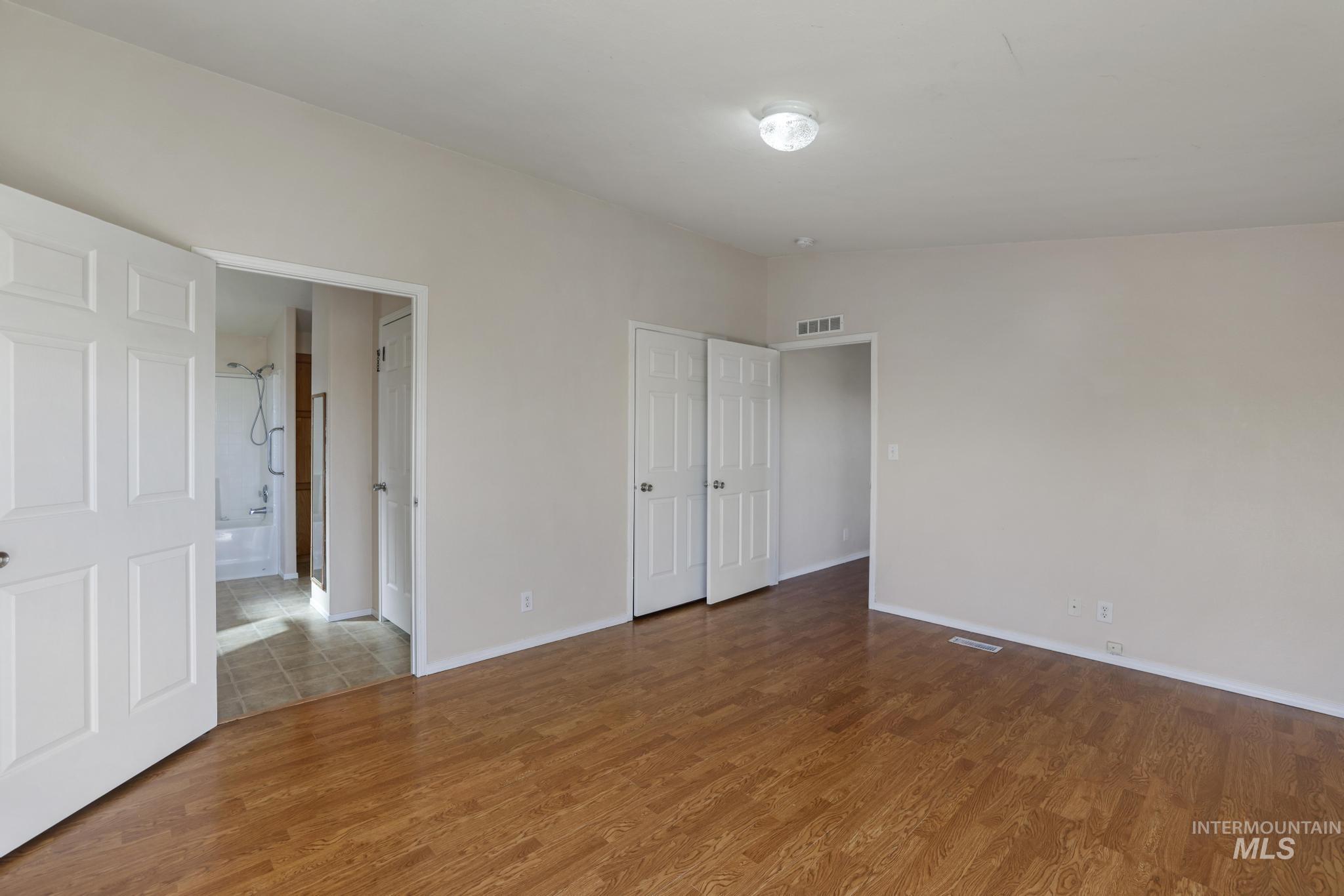 Unfurnished bedroom featuring wood finished floors, connected bathroom, and lofted ceiling