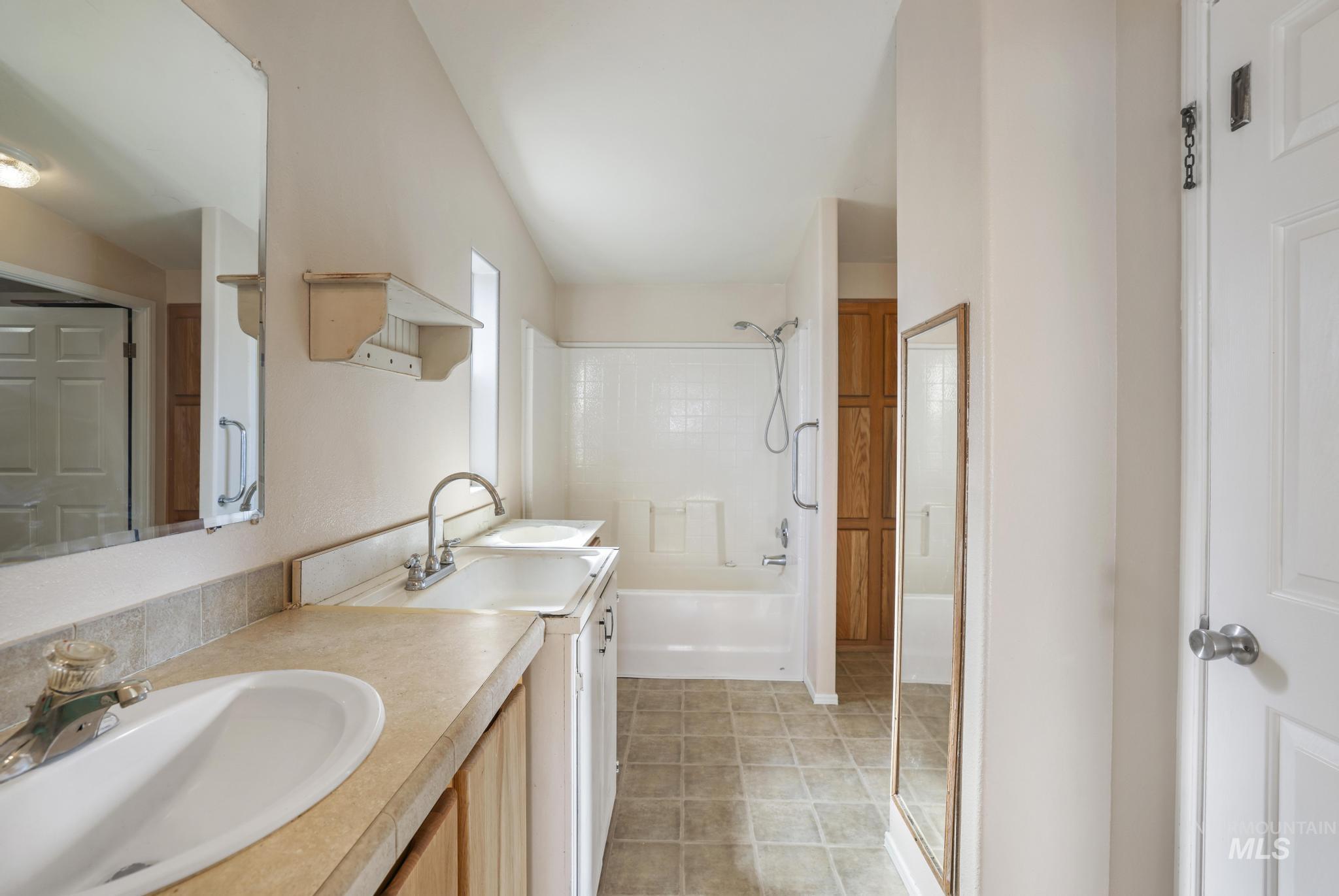 Full bathroom with double vanity, light tile patterned floors, and shower / bath combination