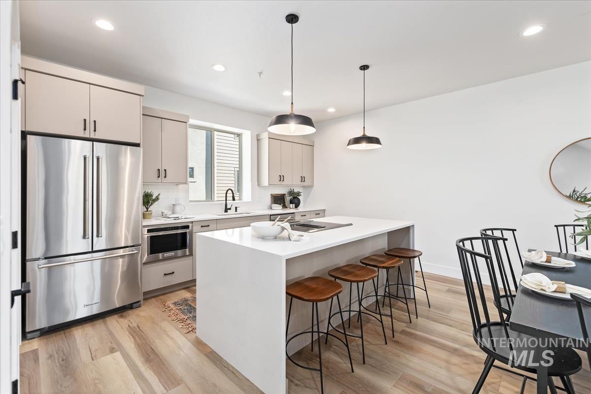 Kitchen with stainless steel appliances, light wood finished floors, a kitchen bar, light countertops, and recessed lighting