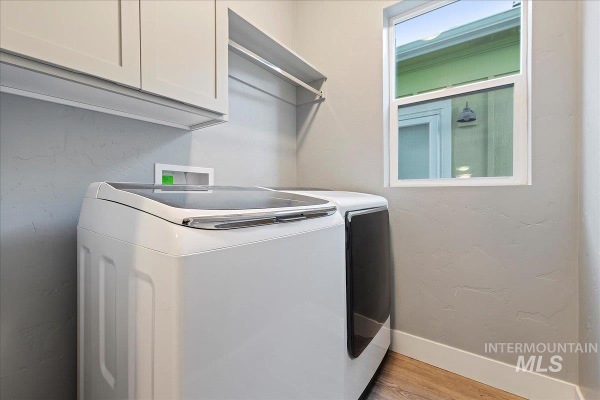 Washroom featuring a textured wall, cabinet space, light wood-type flooring, and washing machine and clothes dryer