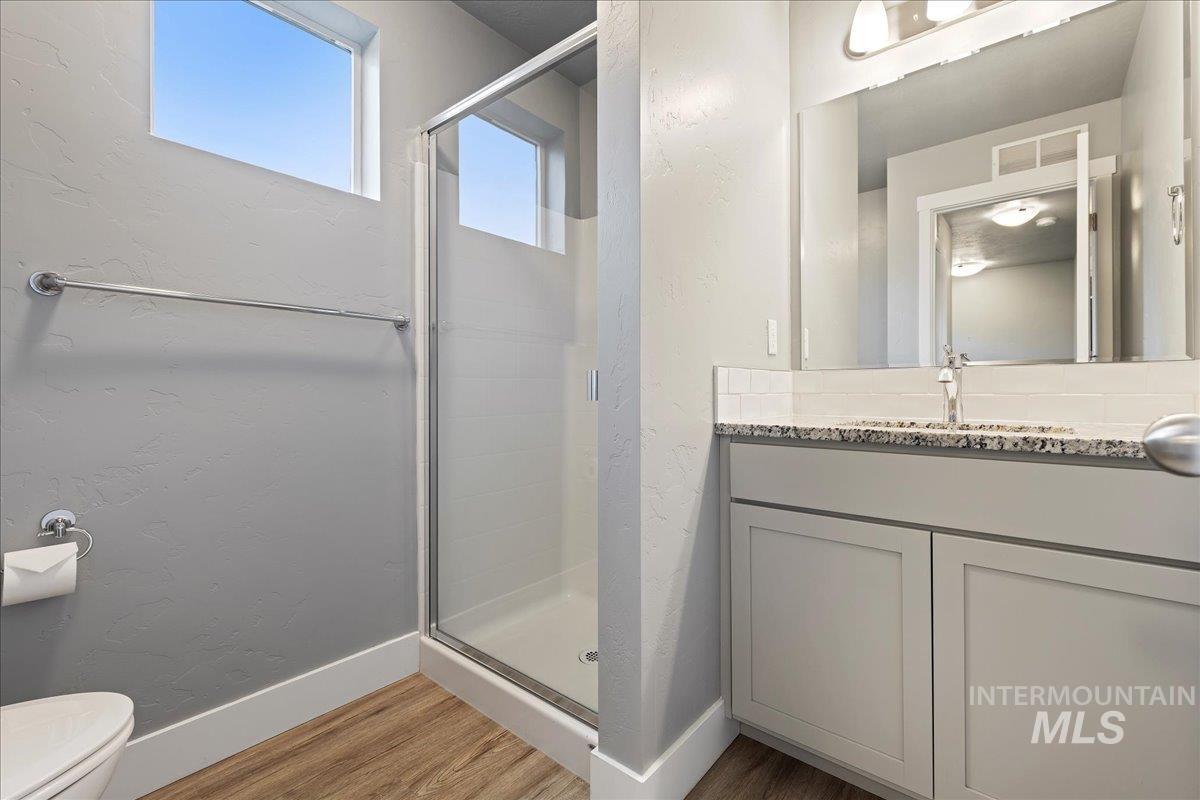 Full bathroom featuring vanity, a textured wall, a stall shower, and light wood-style floors
