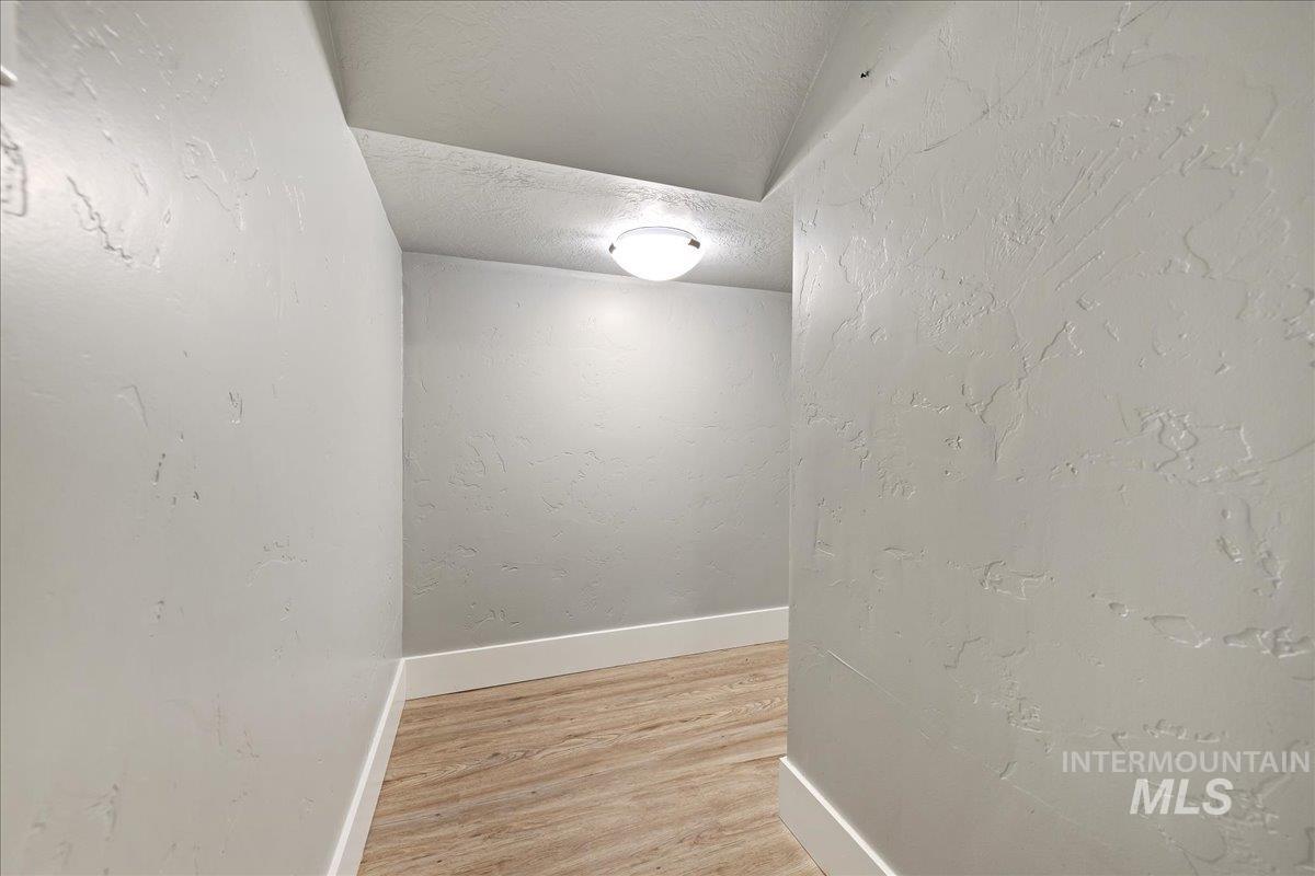 Corridor with a textured wall, a textured ceiling, and light wood-type flooring