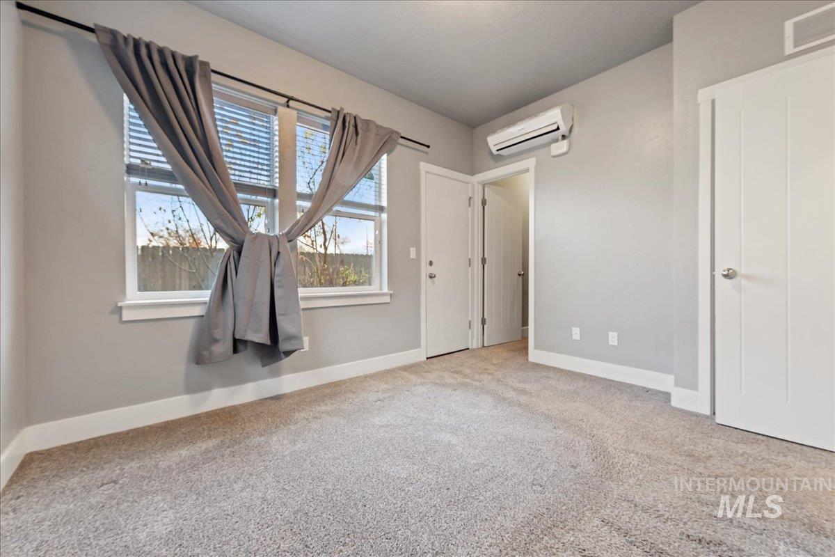 Unfurnished bedroom with light colored carpet and a wall mounted AC