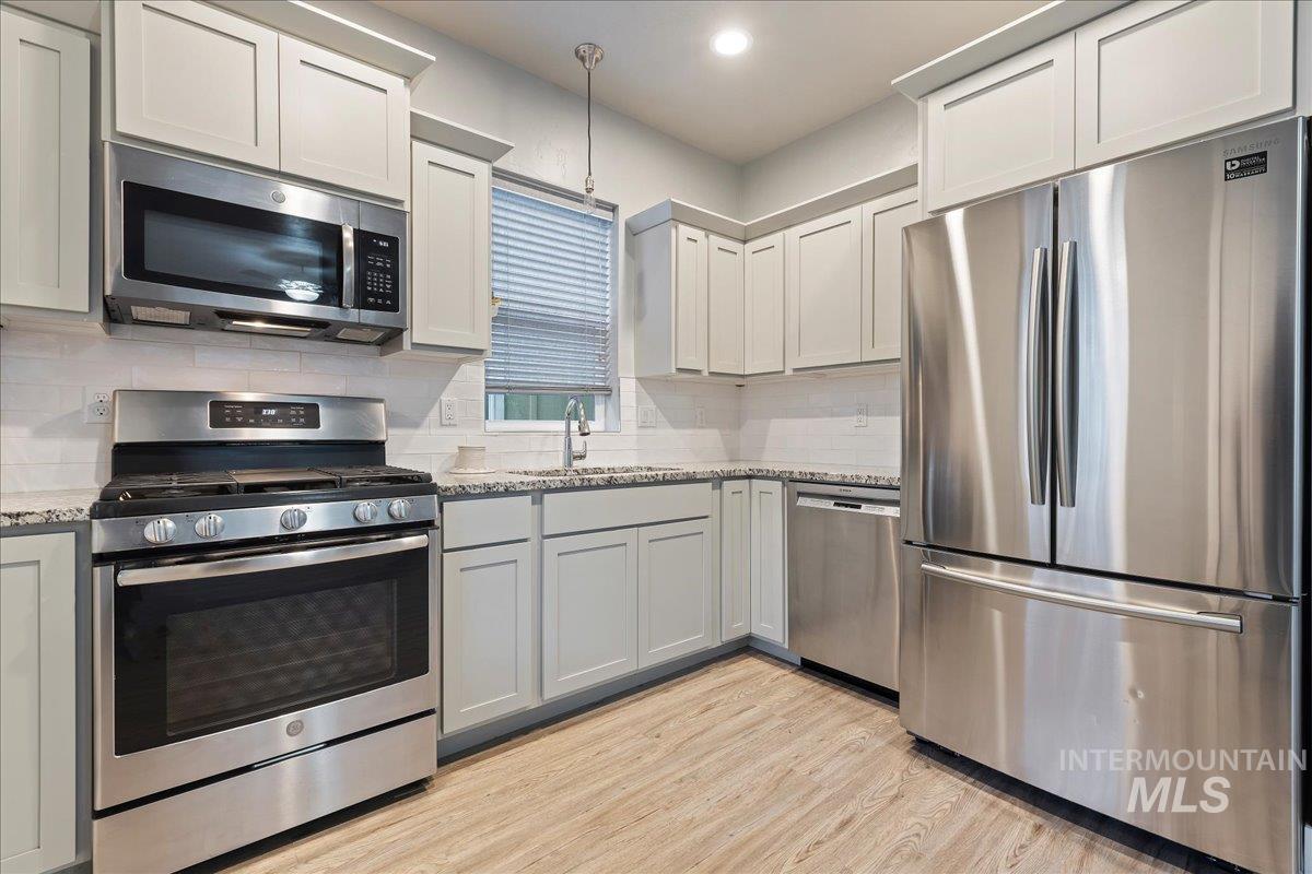 Kitchen featuring stainless steel appliances, tasteful backsplash, light stone counters, light wood-style floors, and pendant lighting