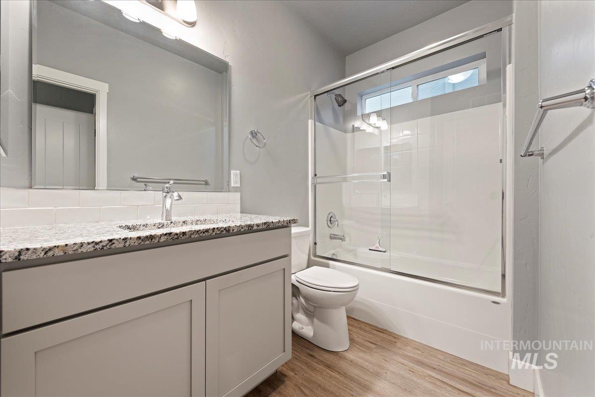 Full bathroom with enclosed tub / shower combo, vanity, and light wood finished floors