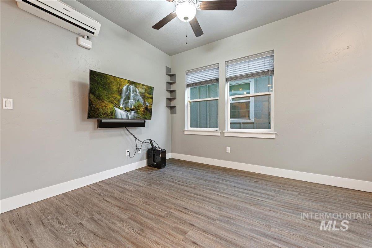 Empty room featuring wood finished floors, a wall mounted air conditioner, and a ceiling fan