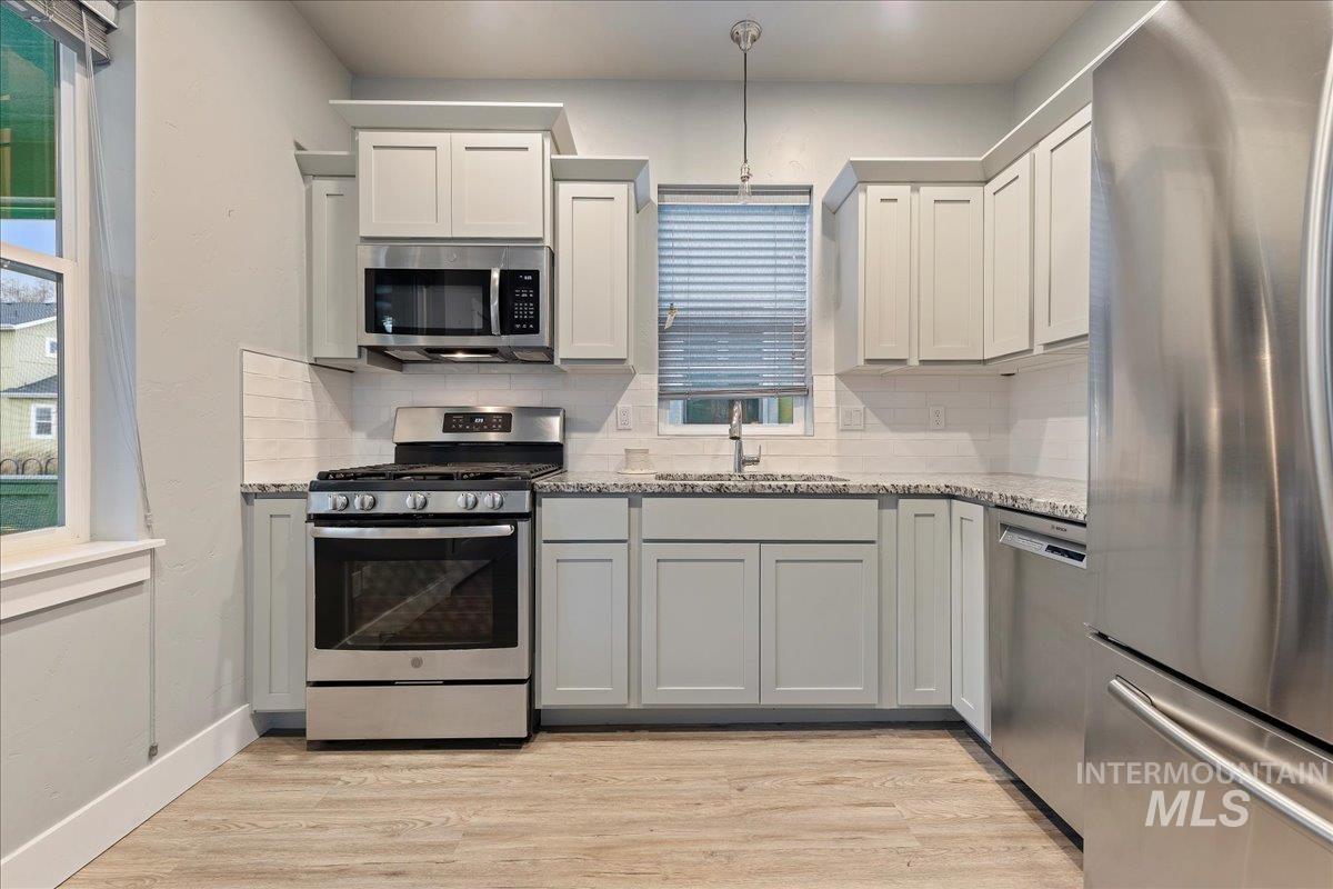 Kitchen featuring appliances with stainless steel finishes, backsplash, light stone counters, light wood-type flooring, and white cabinets