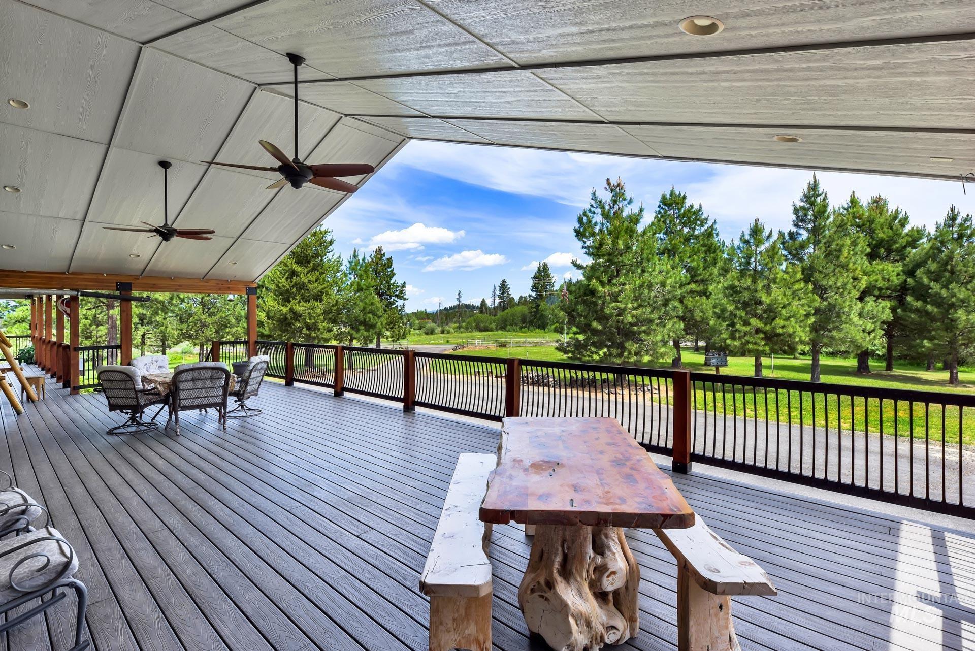Trex deck with ceiling fans, outdoor dining space, and view of scattered trees on side of home