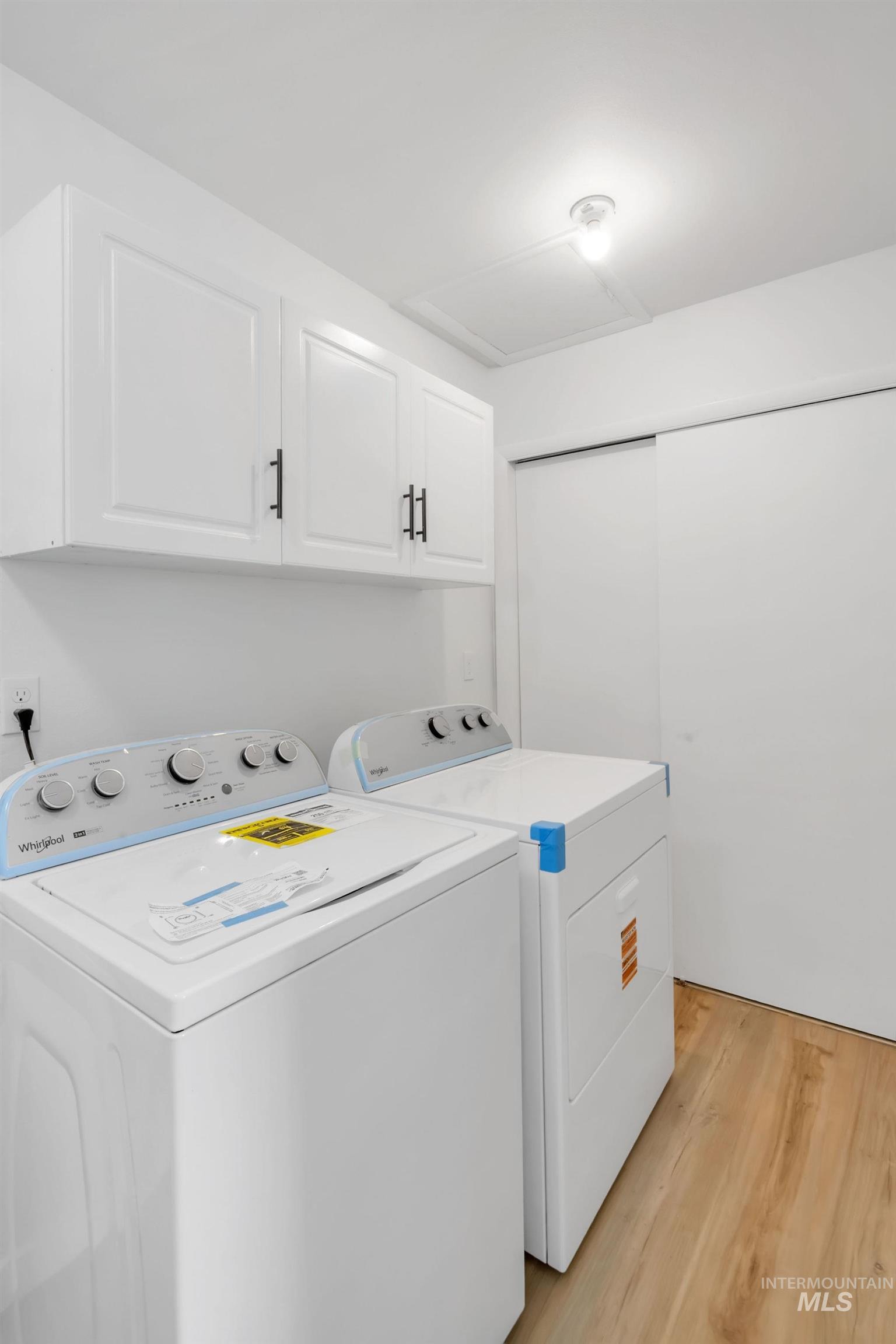 Washroom with cabinet space, washing machine and dryer, and light wood finished floors