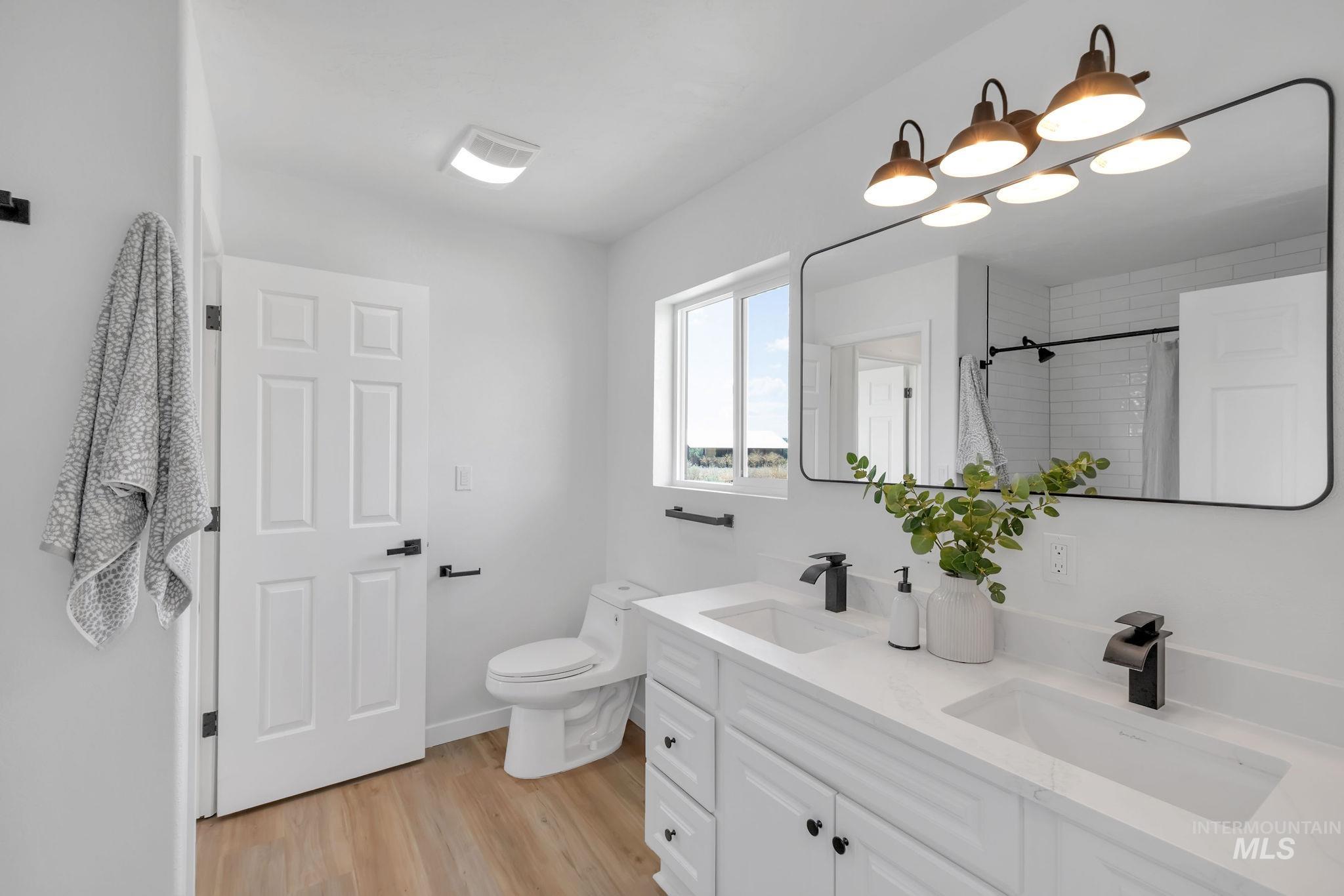 Bathroom featuring wood finished floors, double vanity, and tiled shower
