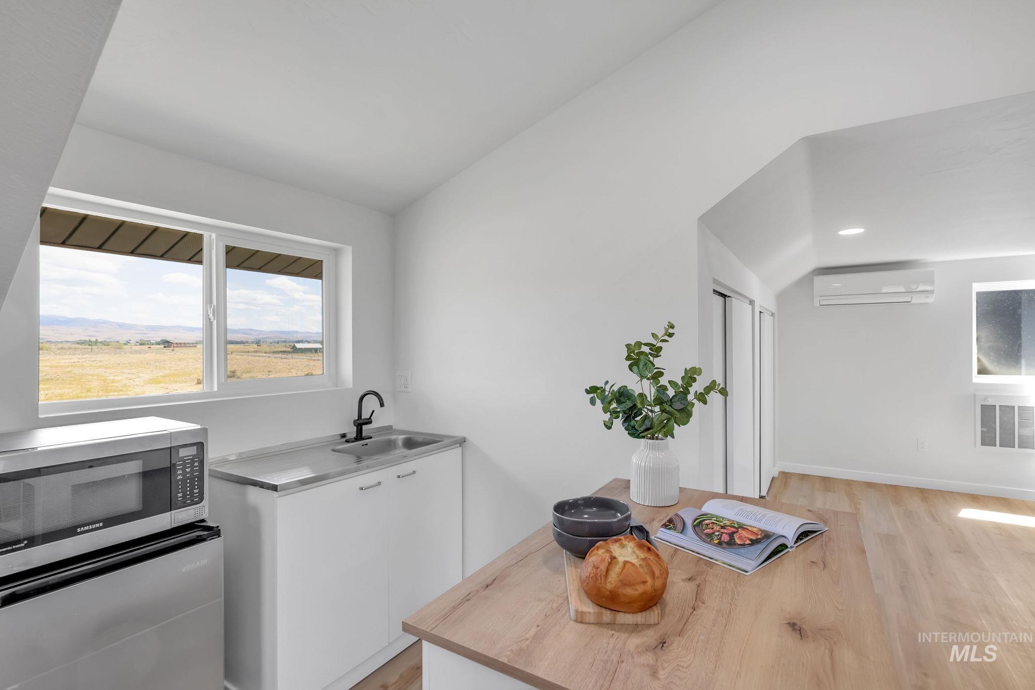 Kitchen with vaulted ceiling, stainless steel microwave, white cabinets, light wood-style flooring, and light countertops