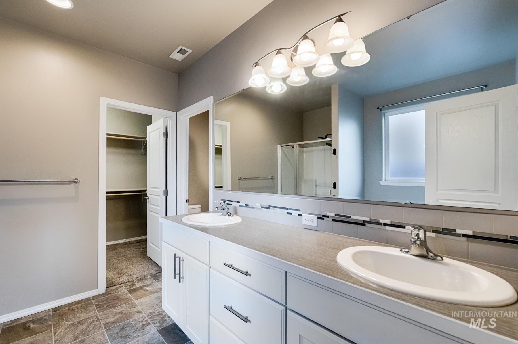 Bathroom with double vanity, a shower stall, a spacious closet, and backsplash