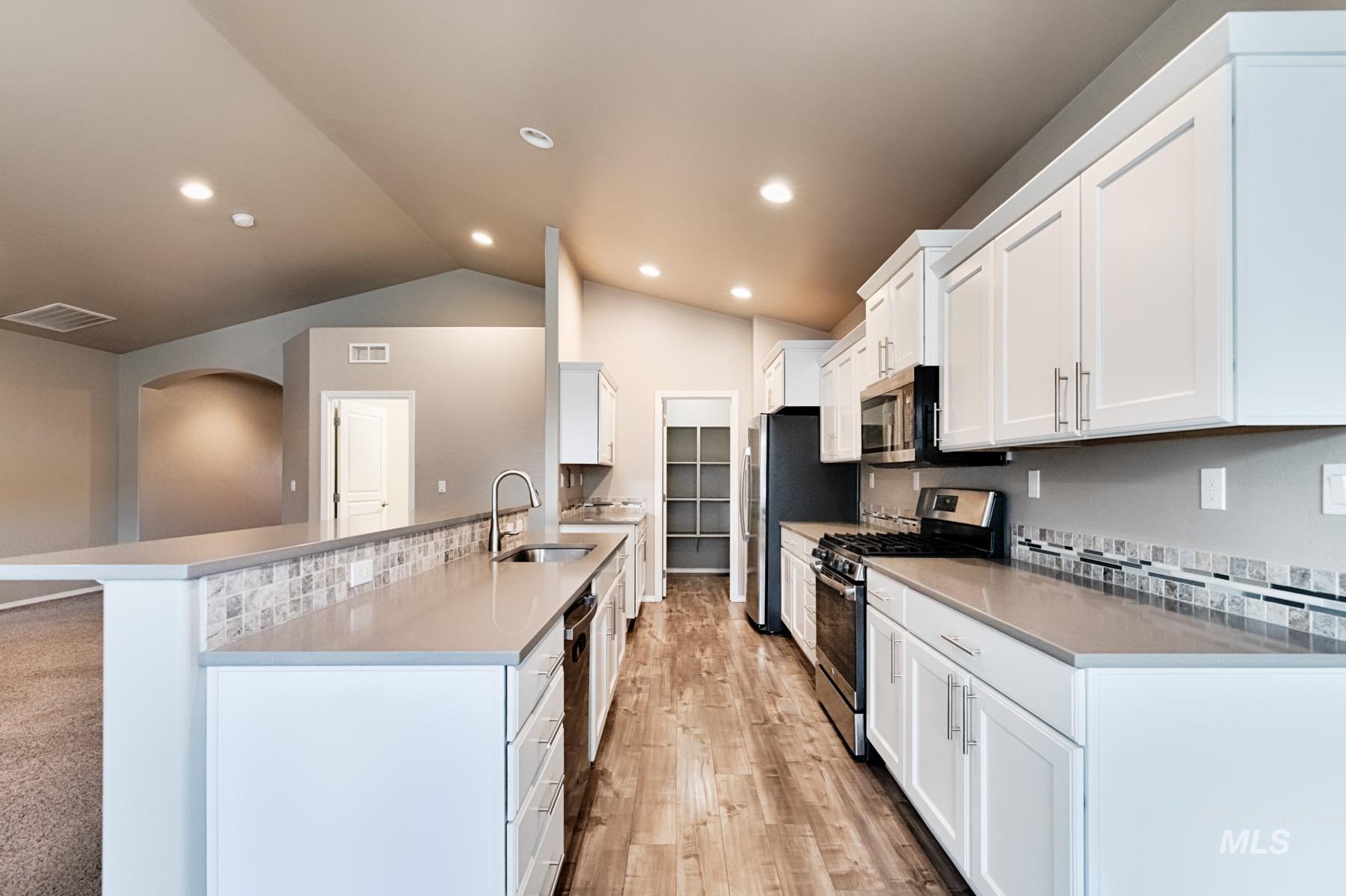 Kitchen with stainless steel appliances, white cabinets, light wood finished floors, a peninsula, and vaulted ceiling
