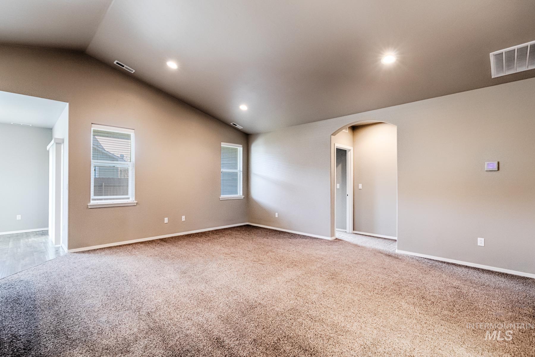 Empty room with arched walkways, light colored carpet, vaulted ceiling, and recessed lighting