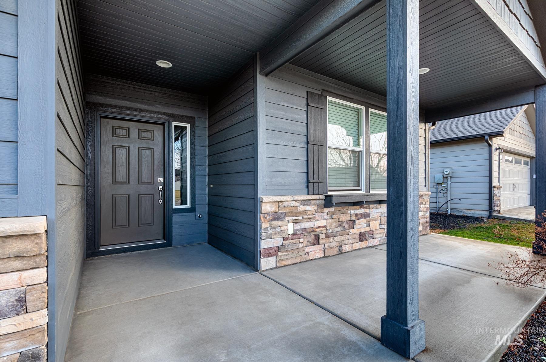 Entrance to property featuring a garage, stone siding, and a porch