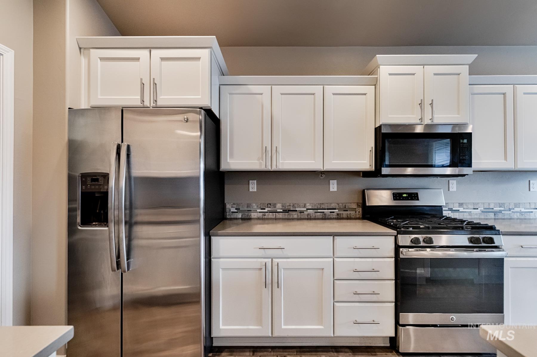 Kitchen with stainless steel appliances, white cabinets, and light countertops