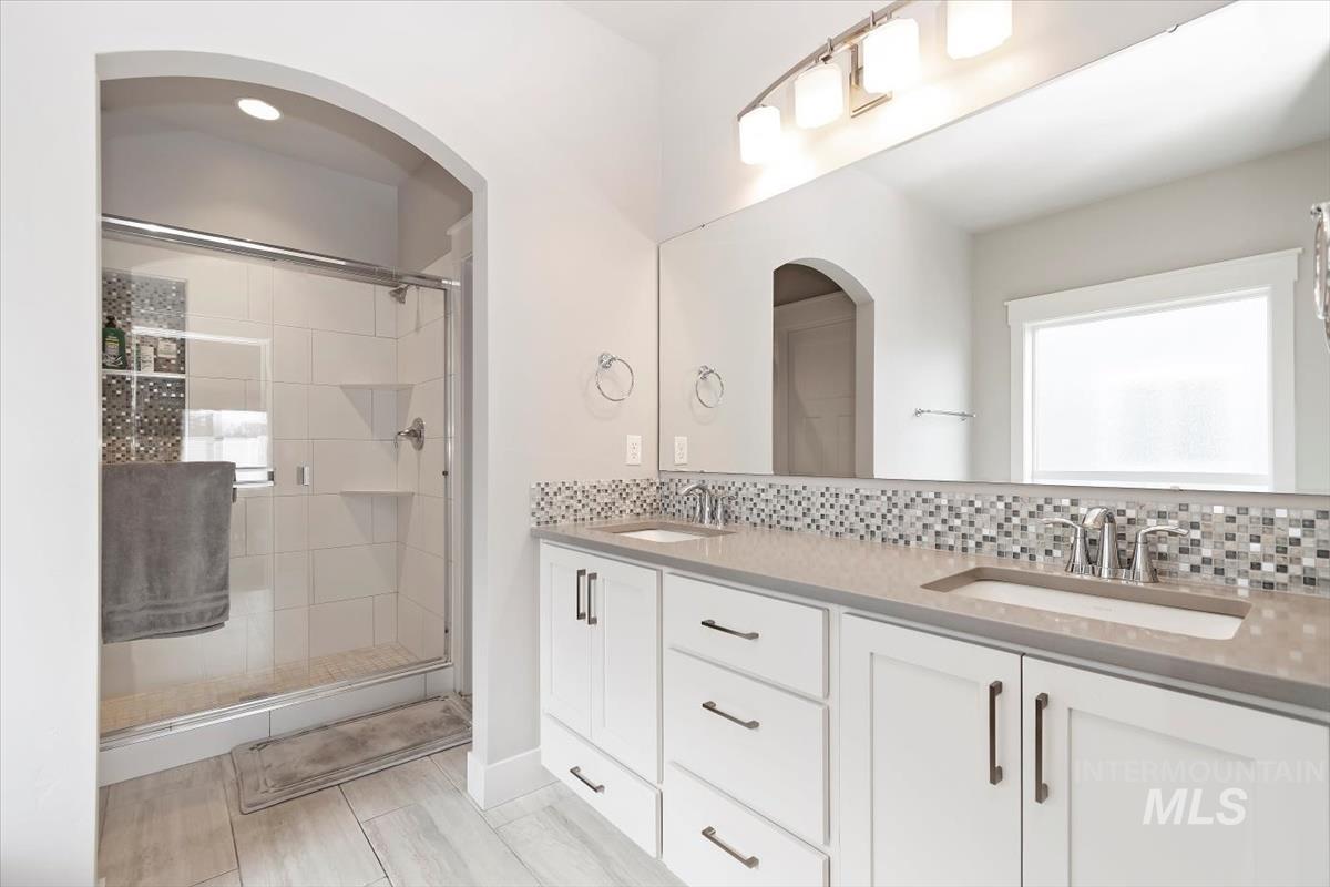 Full bathroom featuring double vanity, a stall shower, and decorative backsplash