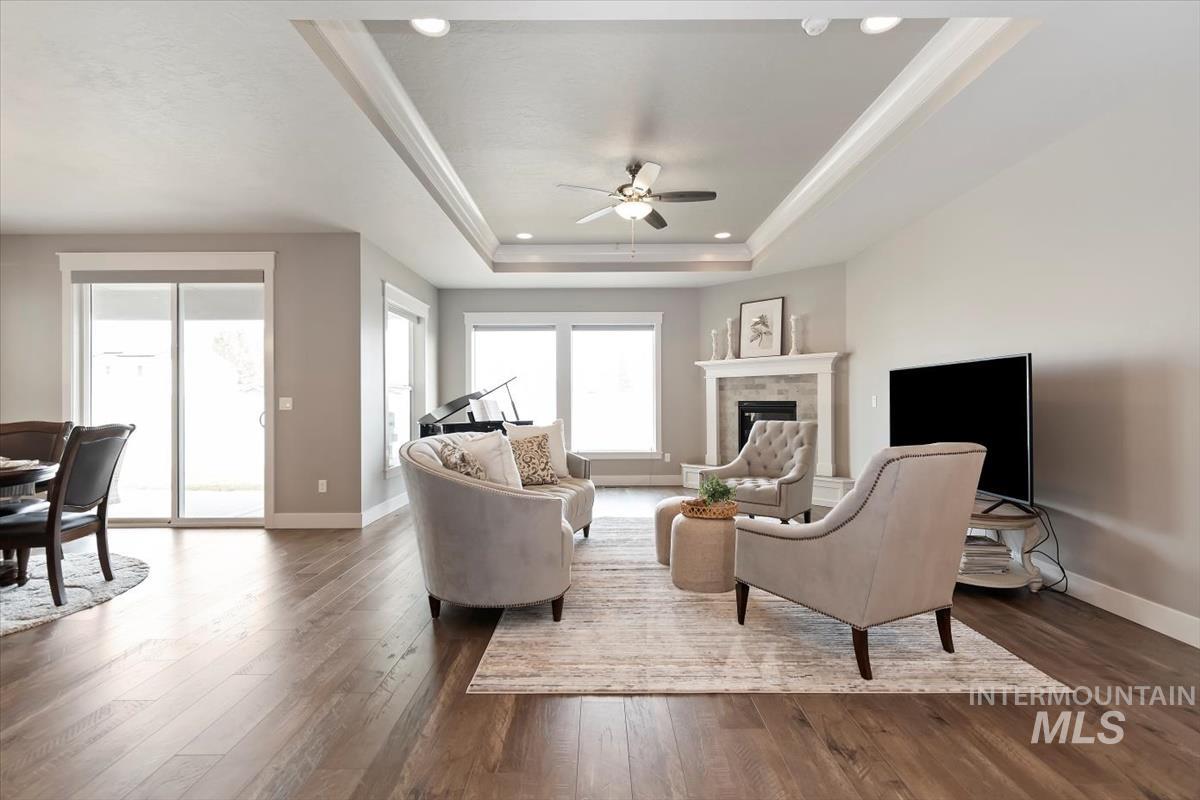 Living room with dark wood-style floors, a raised ceiling, a tiled fireplace, a ceiling fan, and recessed lighting