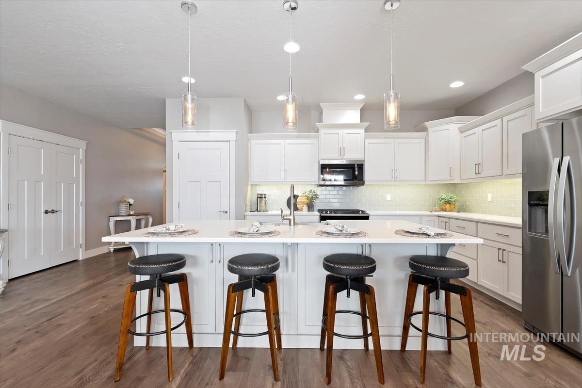 Kitchen with stainless steel appliances, a kitchen breakfast bar, white cabinetry, an island with sink, and dark wood-style floors