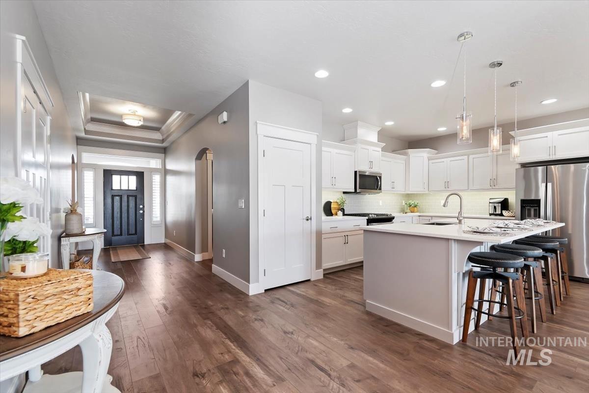 Kitchen featuring appliances with stainless steel finishes, decorative light fixtures, white cabinets, a breakfast bar area, and a center island with sink