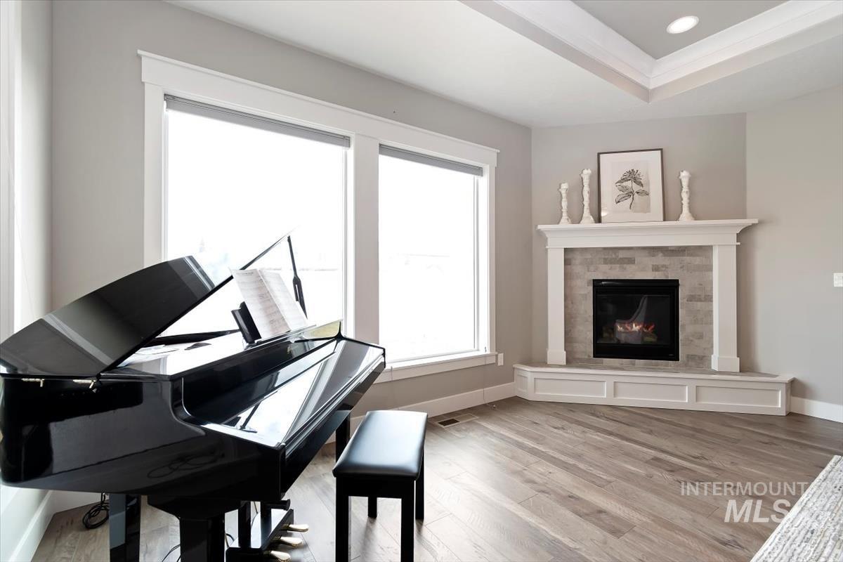 Sitting room with a glass covered fireplace, light wood-type flooring, ornamental molding, a tray ceiling, and recessed lighting
