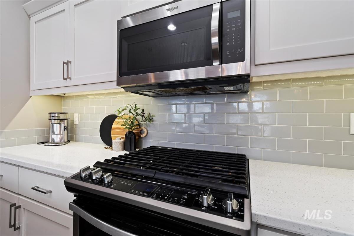 Kitchen with gas range, stainless steel microwave, white cabinetry, and light stone countertops