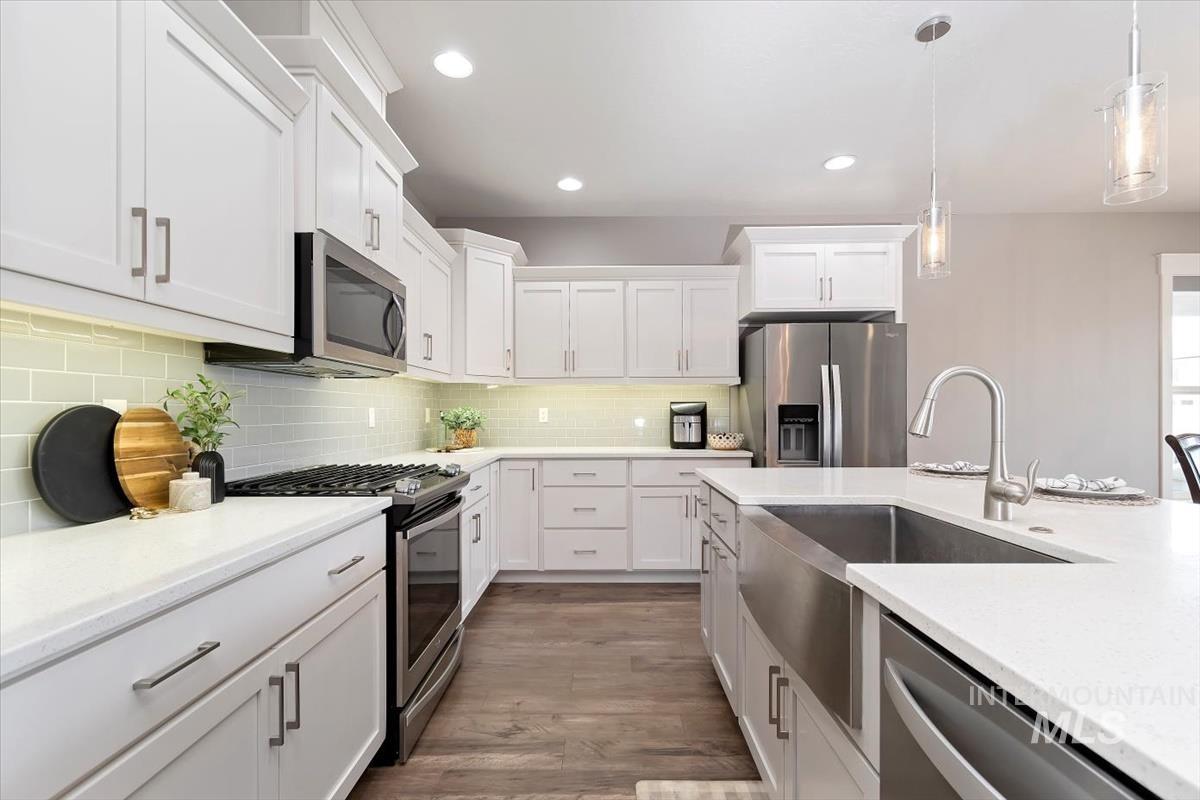 Kitchen featuring stainless steel appliances, pendant lighting, white cabinets, light wood-style floors, and light stone counters