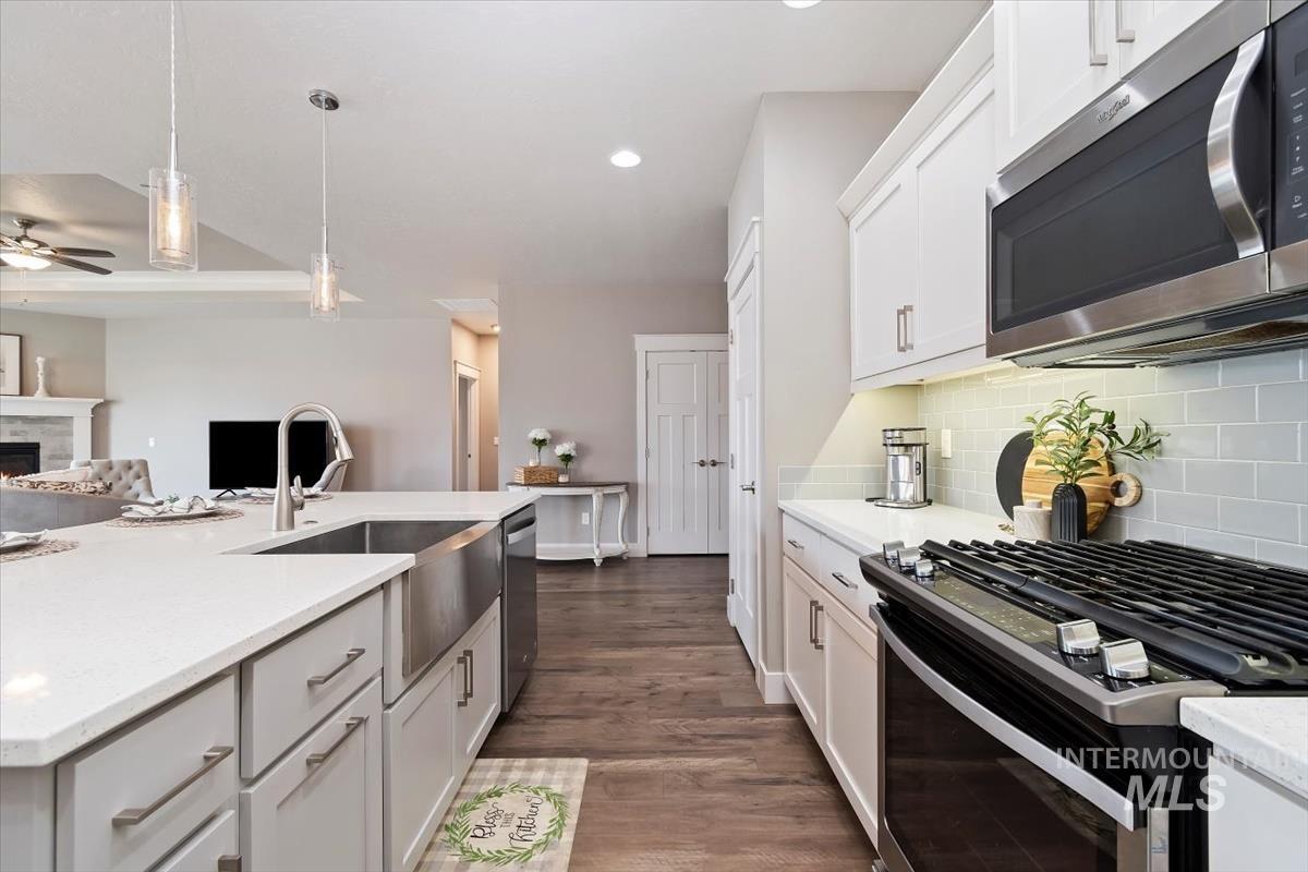 Kitchen featuring stainless steel appliances, decorative light fixtures, white cabinets, a lit fireplace, and dark wood-style flooring