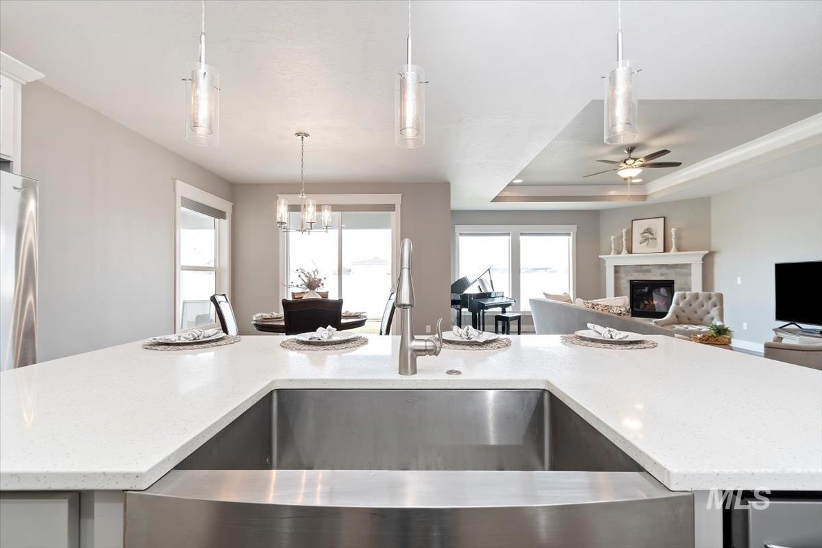 Kitchen with light stone counters, decorative light fixtures, a tray ceiling, a glass covered fireplace, and open floor plan