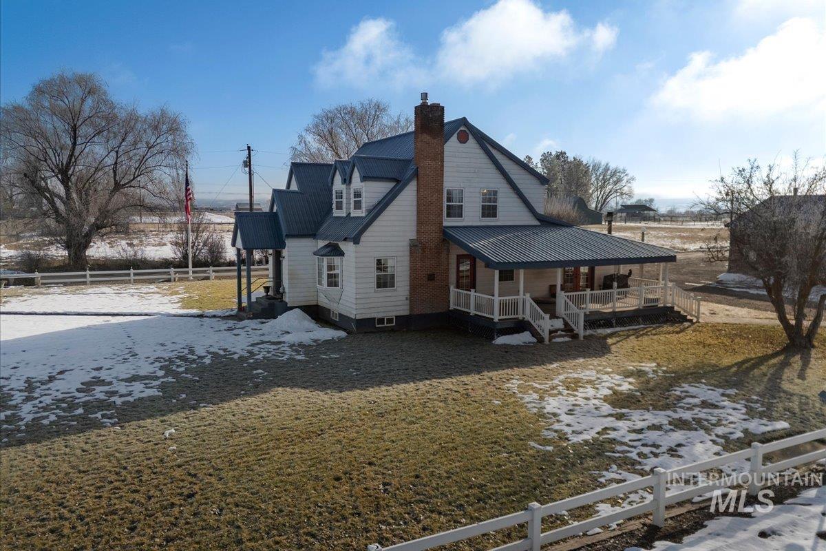 Snow covered back of property with a metal roof, a chimney, and a porch