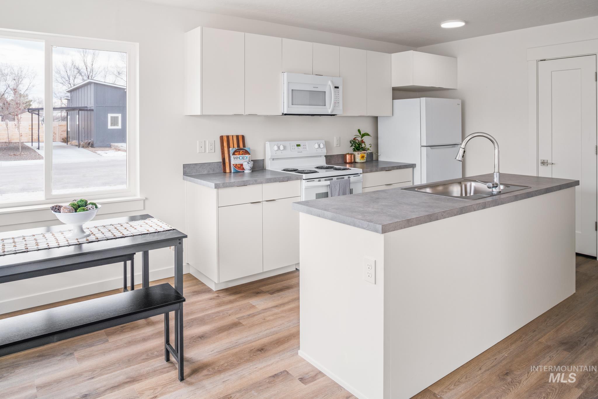 Kitchen with white cabinetry, white appliances, light wood-style flooring, and a kitchen island with sink
