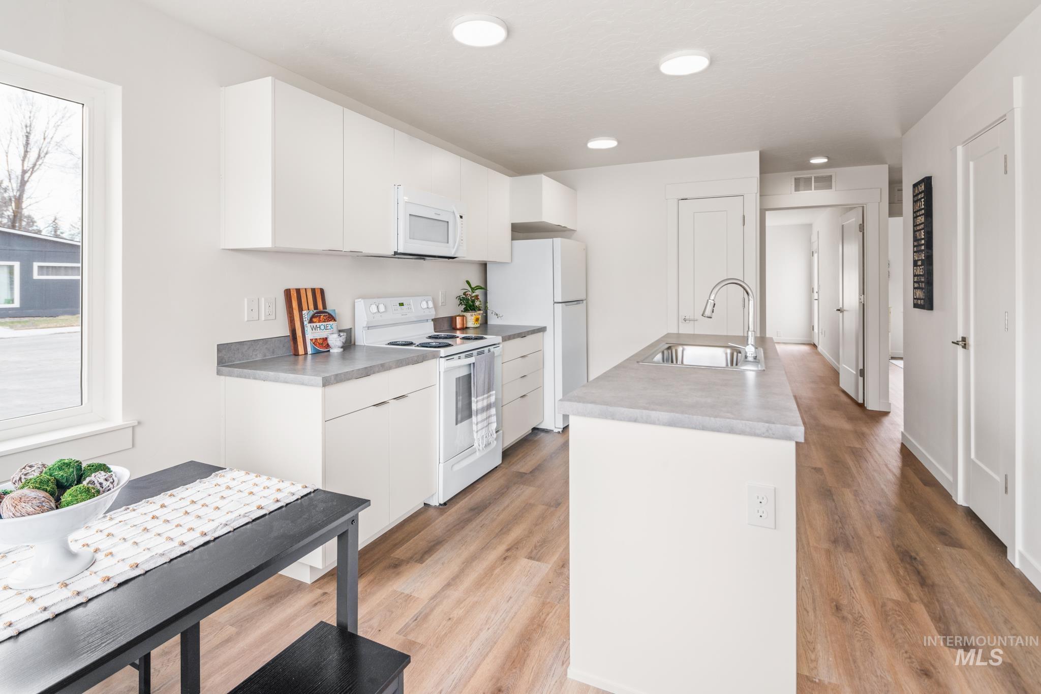 Kitchen with white appliances, white cabinetry, an island with sink, light wood finished floors, and recessed lighting