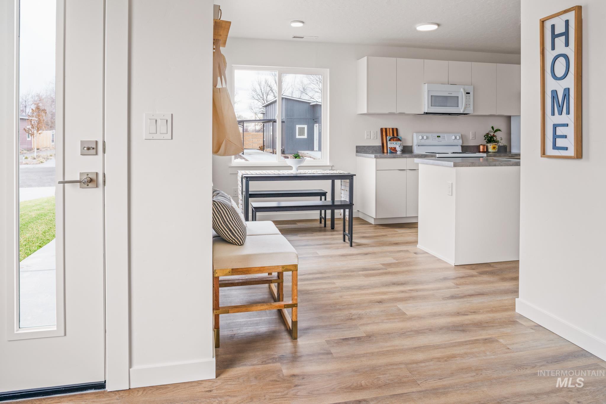 Kitchen with white cabinets, dark countertops, white appliances, light wood finished floors, and recessed lighting