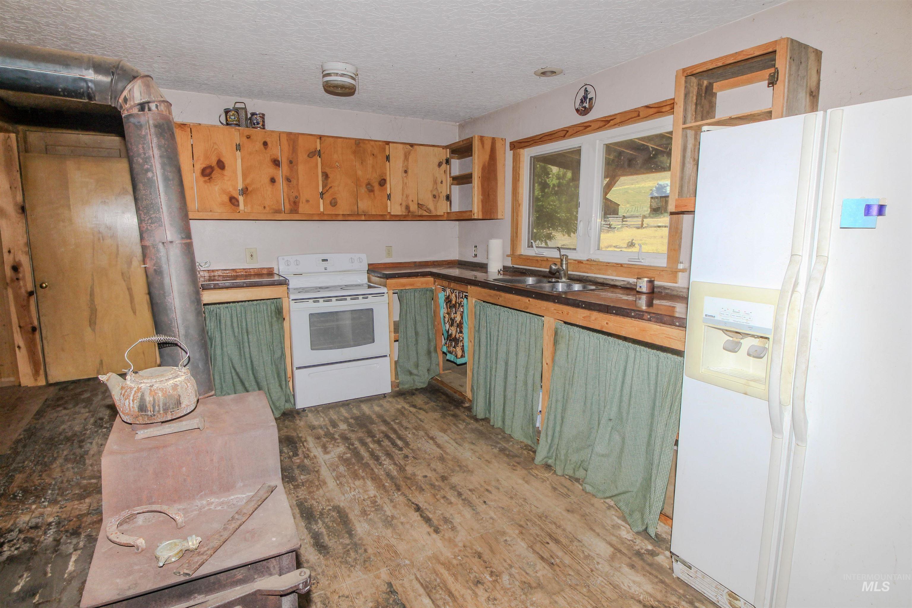 Kitchen featuring white appliances, dark countertops, green cabinets, dark wood-type flooring, and a textured ceiling