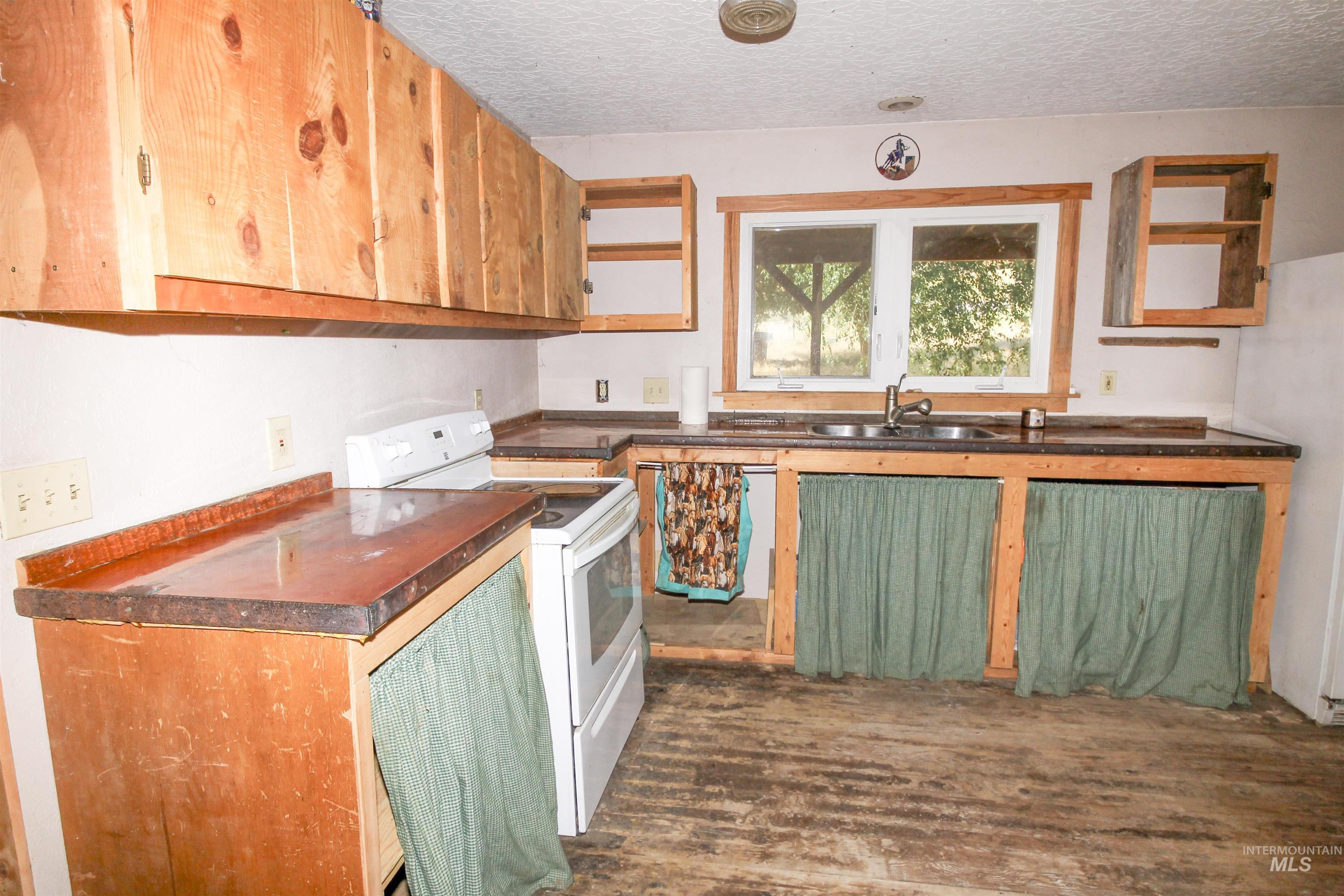 Kitchen with white appliances, a textured ceiling, dark wood-style flooring, dark countertops, and brown cabinetry