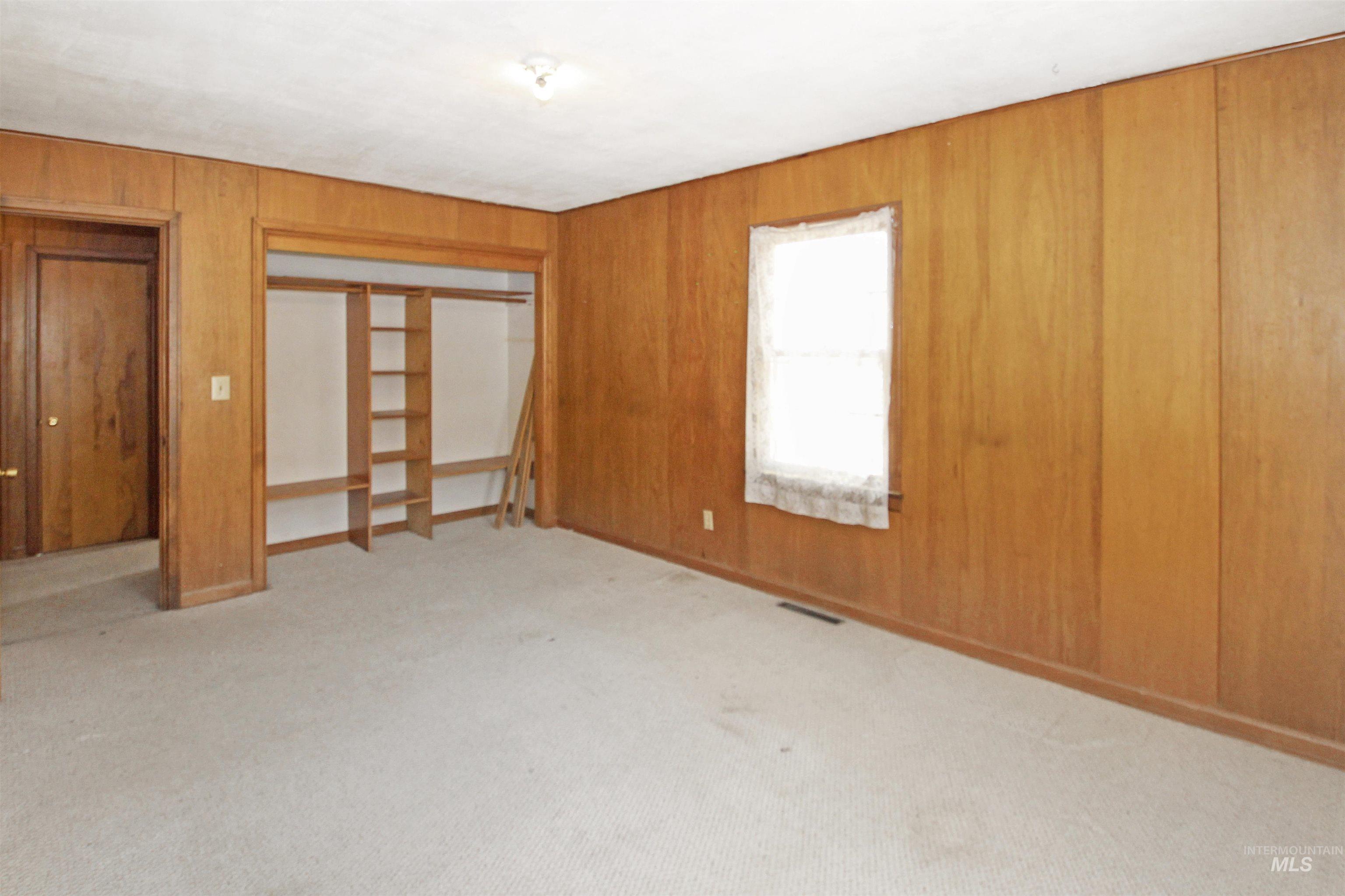 Unfurnished bedroom with wooden walls, light colored carpet, and a closet