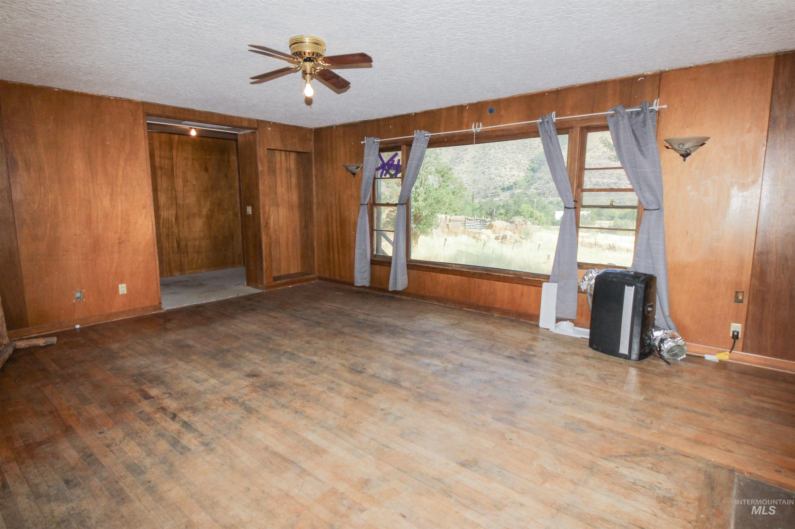 Unfurnished living room featuring wooden walls, wood finished floors, ceiling fan, and a textured ceiling