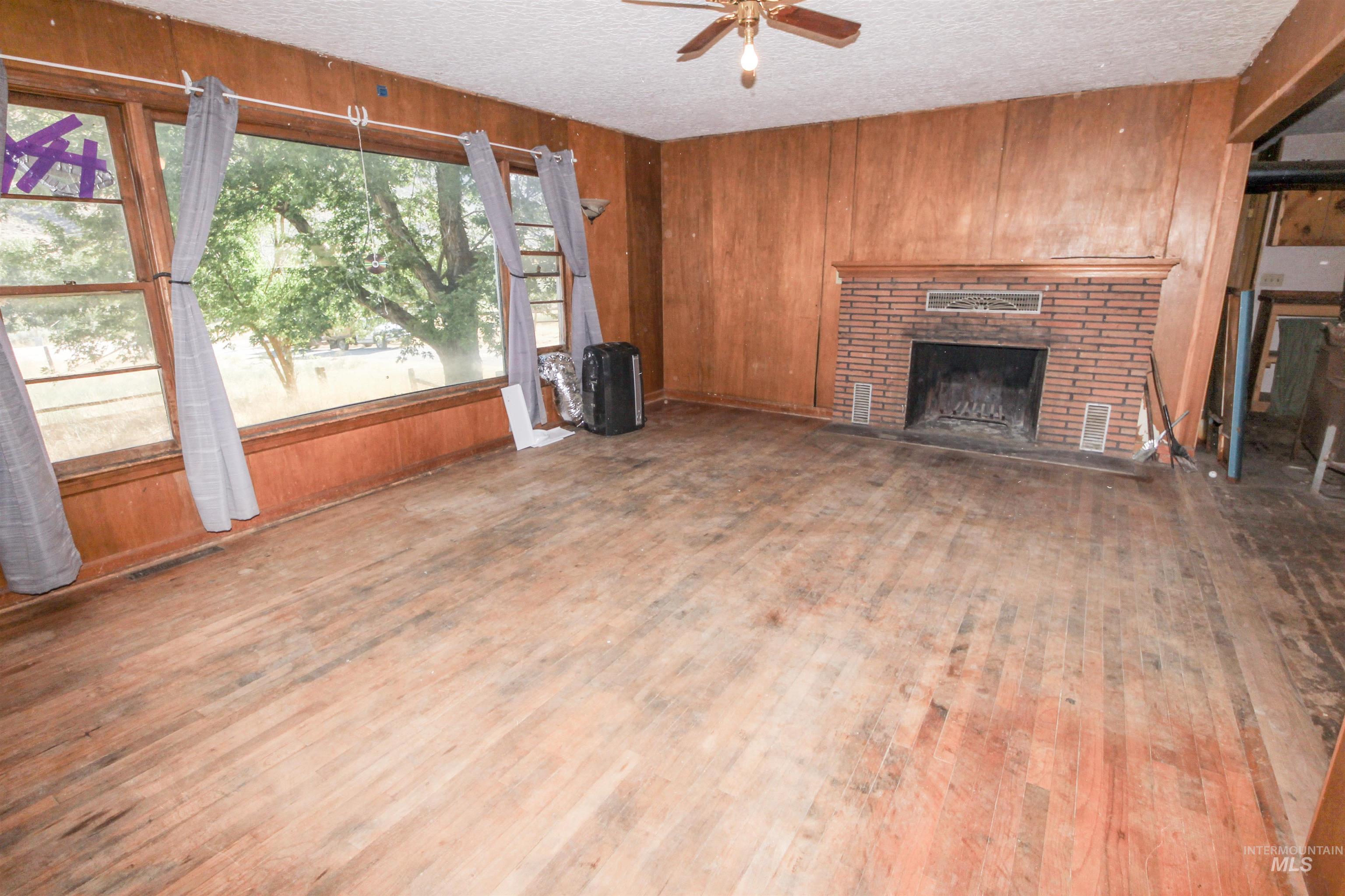 Unfurnished living room featuring wooden walls, a fireplace, a textured ceiling, wood finished floors, and ceiling fan