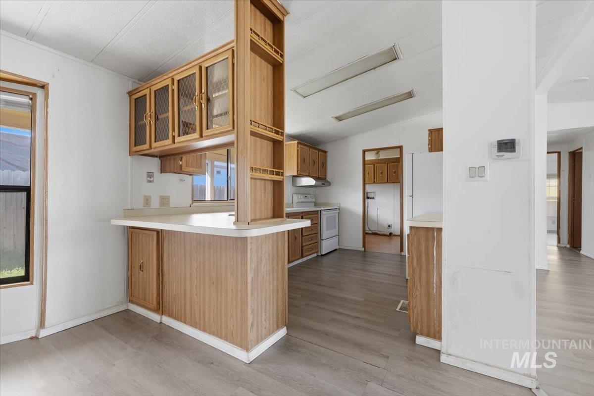 Kitchen featuring wood finish cabinetry, light countertops, white appliances, glass fronted cabinets, and a peninsula