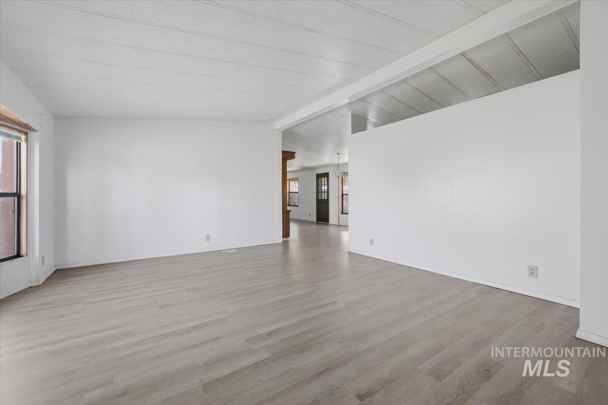 Empty room with vaulted ceiling with beams and light wood-style floors