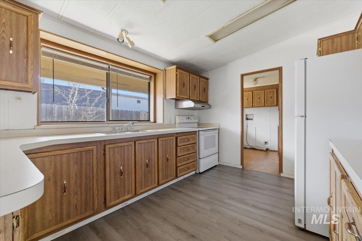 Kitchen with white appliances, light countertops, dark wood-type flooring, wood finish cabinetry, and vaulted ceiling