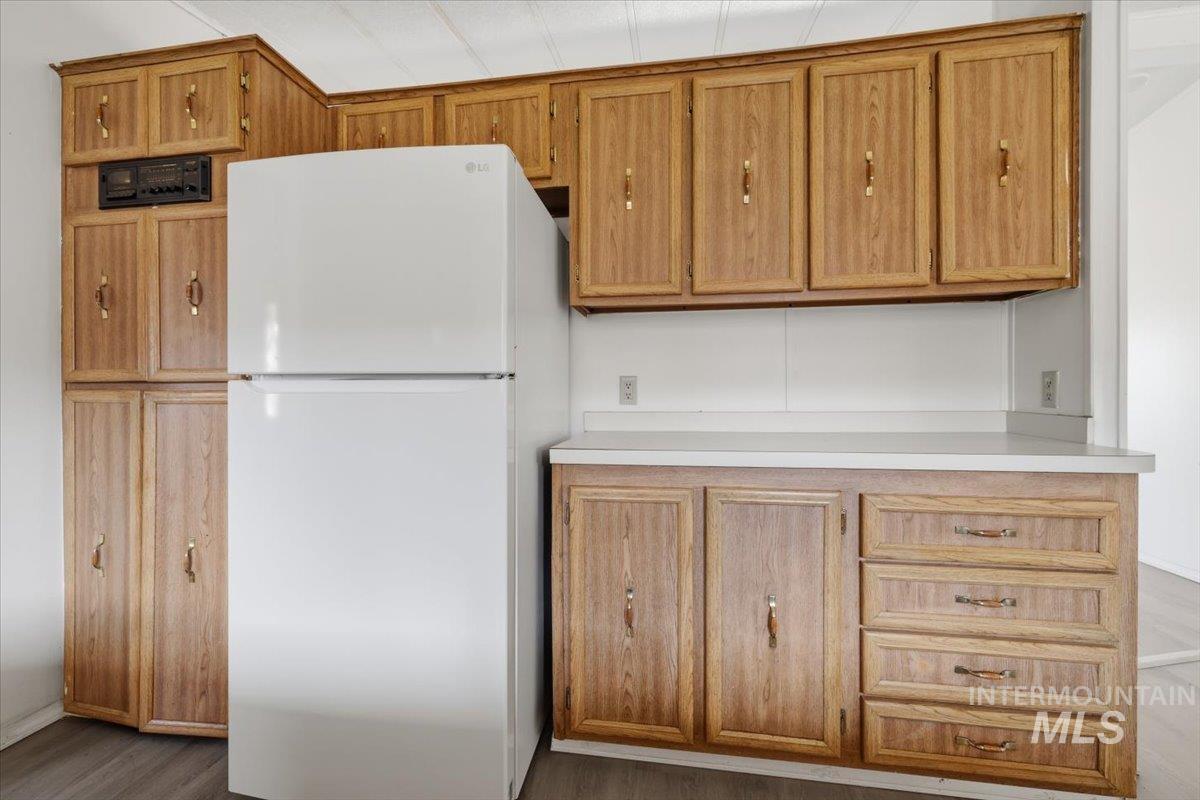 Kitchen with freestanding refrigerator, light countertops, dark wood-style floors, and wood finish cabinets
