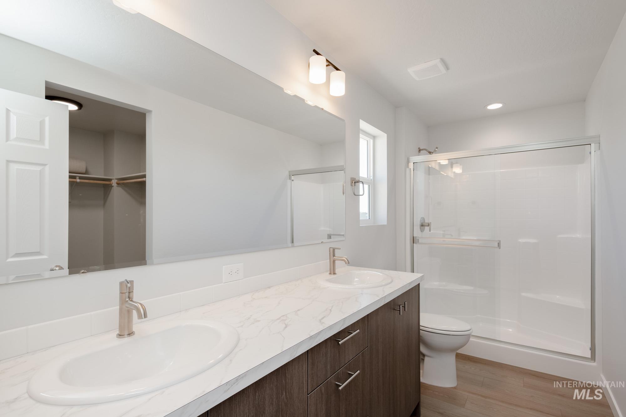 Full bath featuring a shower stall, light wood-style flooring, double vanity, a spacious closet, and recessed lighting