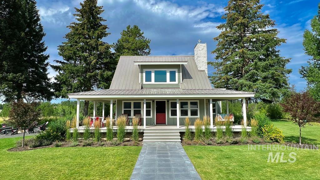 Farmhouse inspired home featuring a porch, a front yard, a chimney, and a metal roof