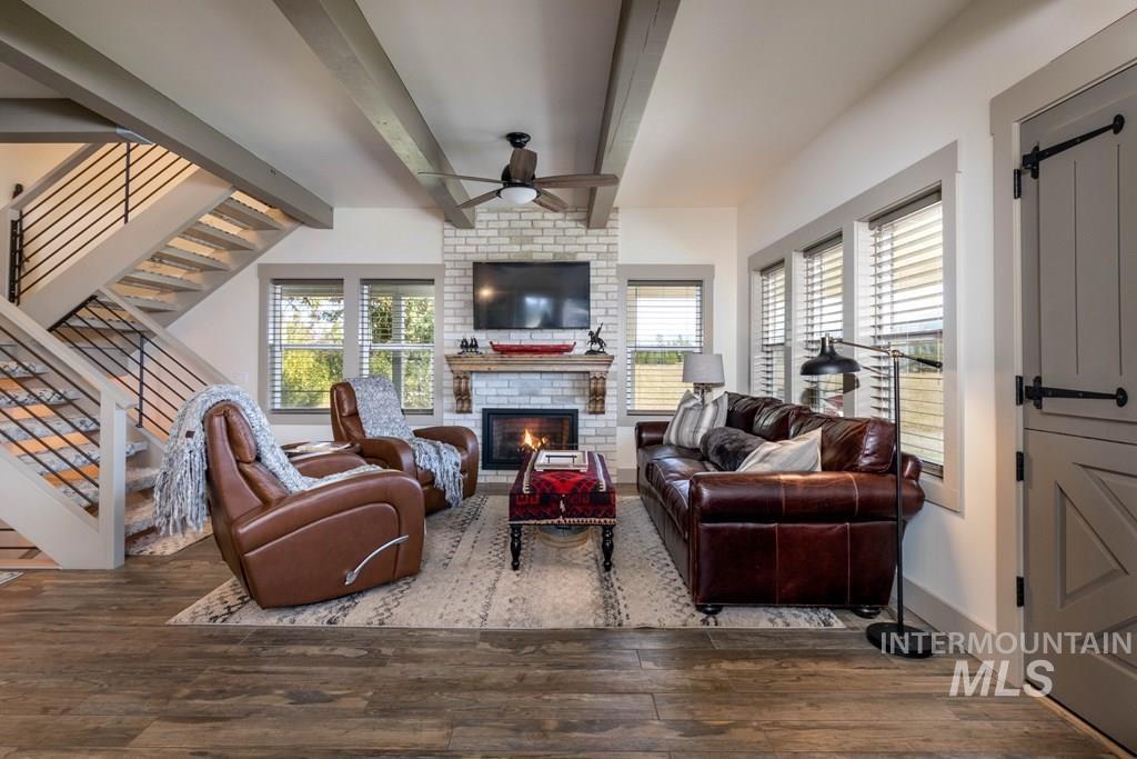 Living room featuring beam ceiling, a barn door, stairway, wood finished floors, and ceiling fan