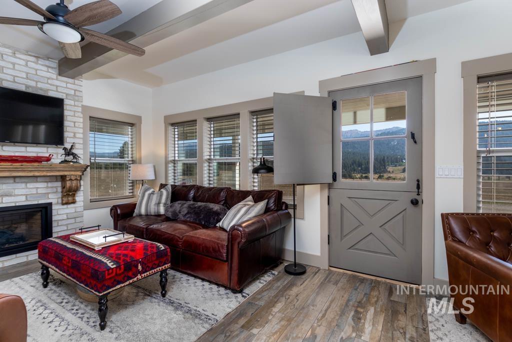 Living area featuring light wood finished floors, beamed ceiling, a fireplace, and a ceiling fan