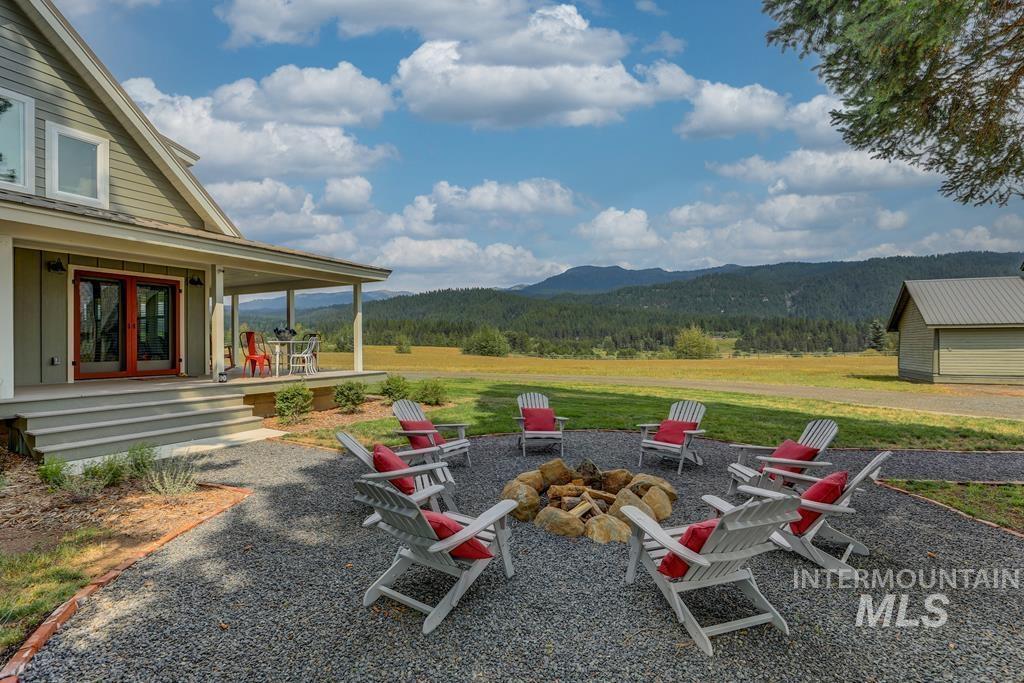View of green lawn with an outdoor fire pit, a forest view, a mountain view, covered porch, and a patio